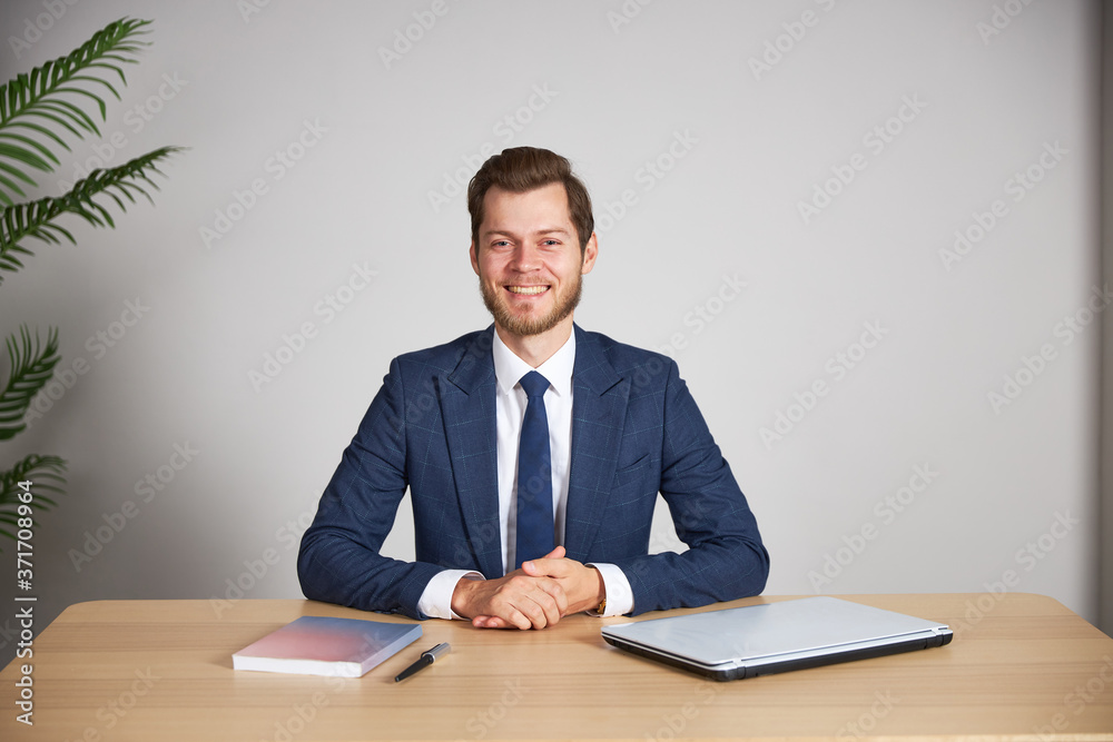 The businessman sits at his desk on a white blank background, crosses his arms and looks into the camera, smiling. The businessman sits at his desk on a white blank background, crosses his arms and looks into the camera, smiling.