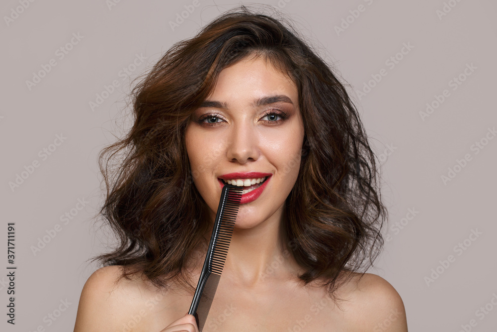 Portrait of a beautiful brunette with lush hair and makeup. Red lipstick and short hair. Smiling holding hairbrush Portrait of a beautiful brunette with lush hair and makeup. Red lipstick and short hair. Smiling holding hairbrush