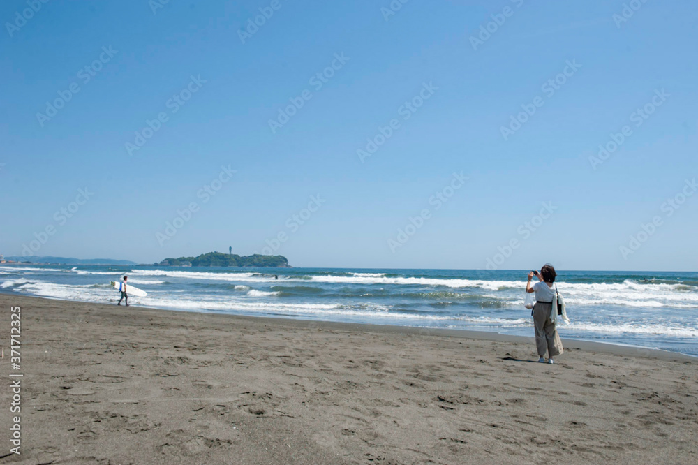 湘南　鵠沼海岸と江ノ島と浜辺でスマホで写真を撮影する若い女性