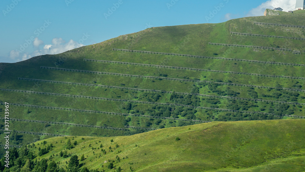Many avalanche barriers on a steep mountain slope. Prevention for the falling of snow avalanches towards the villages located at the bottom of the valley. Summer view
