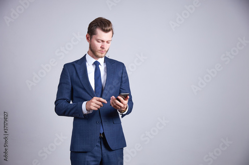 A businessman in a blue business office suit holds his phone, looks at it and presses a button.
