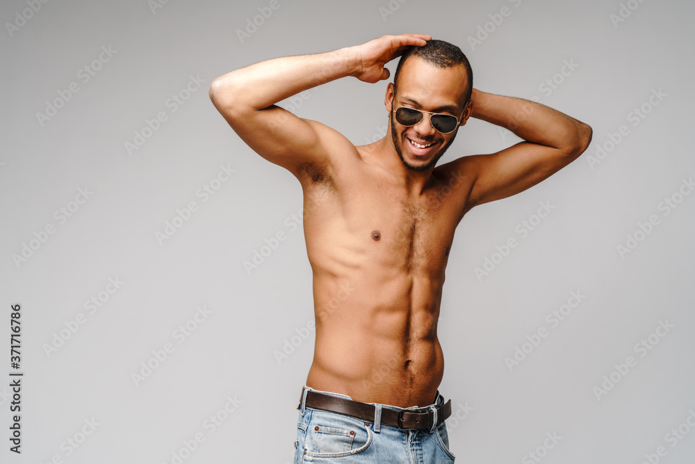 Sexy young muscular african american man shirtless wearing sunglasses over light grey background