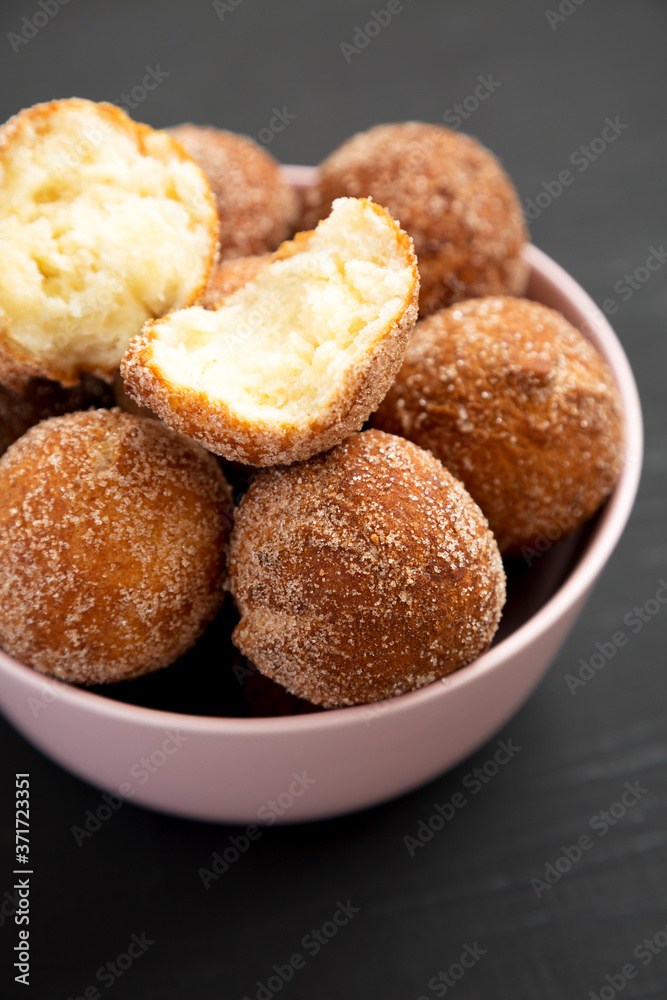 Homemade Fried Donut Holes in a pink bowl on a black background, side view.
