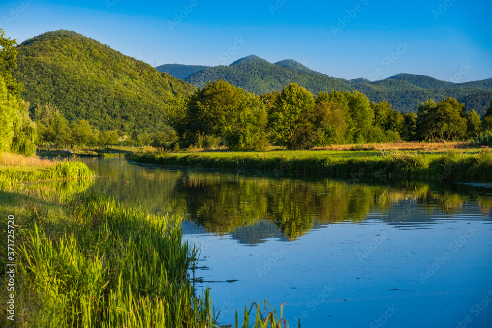Beautiful Gacka river flowing between green fields, summer view, Lika region of Croatia