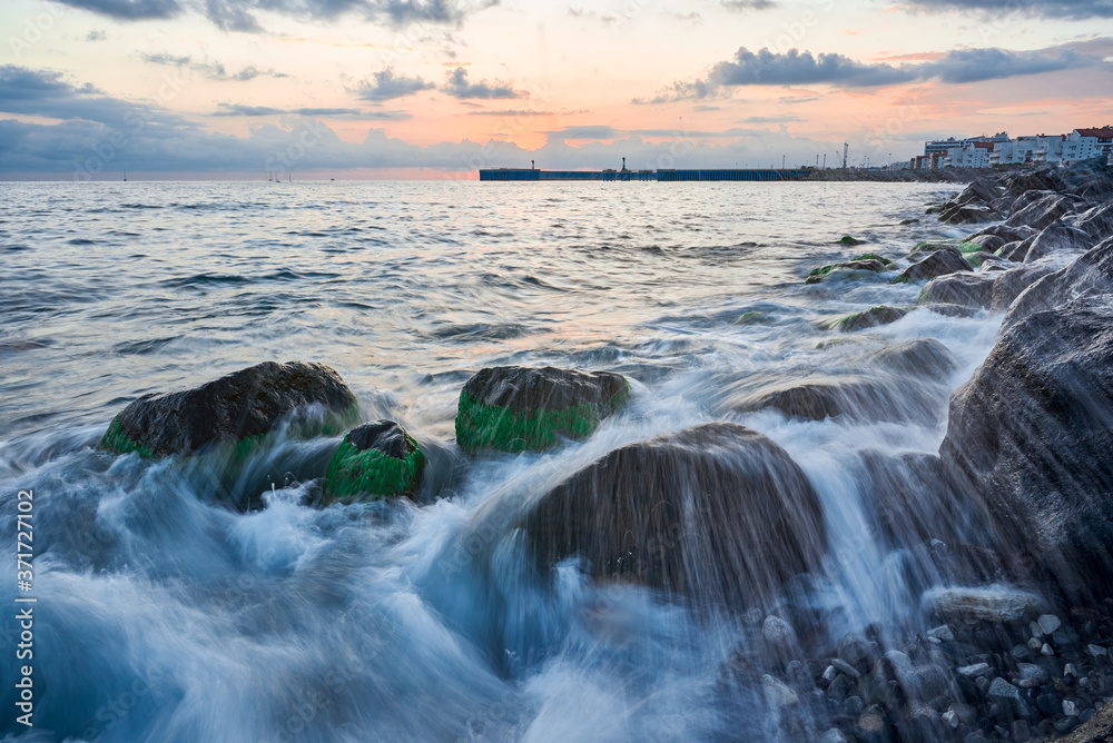 Long exposure of the coastal landscape of Imereti Adler beach with warm evening light, when the waves wash over rocks covered with seaweed Long exposure of the coastal landscape of Imereti Adler beach with warm evening light, when the waves wash over rocks covered with seaweed
