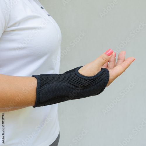Black wrist brace or corset is worn on women's hand for treatment of carpal tunnel syndrome or median nerve compression, numbness hand