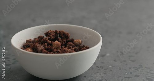 chocolate granola with nuts in white bowl on terrazzo surface