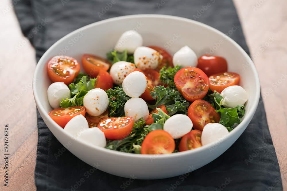 Salad with kale, tomatoes and mozzarella in white bowl Salad with kale, tomatoes and mozzarella in white bowl
