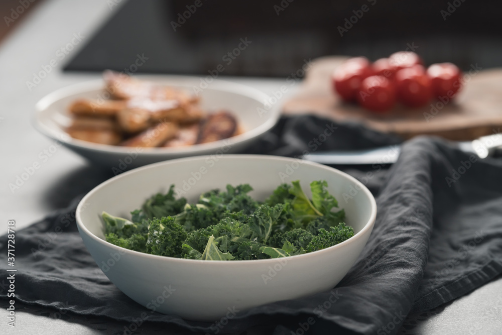 kale salad leaves in white bowl on linen napkin with other ingredients on background