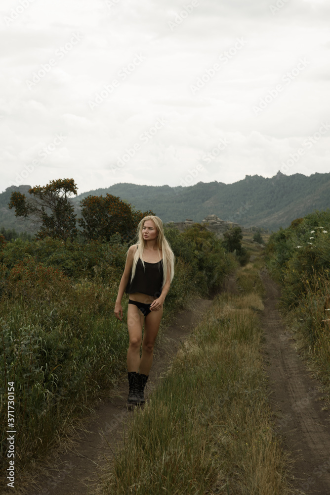 Naklejka premium Stylish girl in black clothes goes against the backdrop of a beautiful landscape