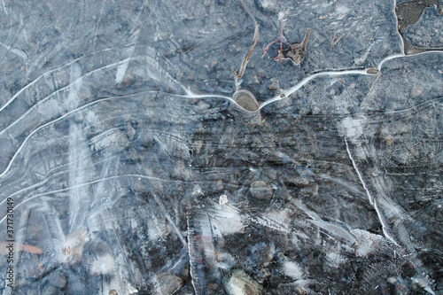 Pebbles can be seen through the crust of ice. Under the first crust of ice on a puddle, pebbles are visible. The first thin crust of ice on a puddle, transparent and tender.