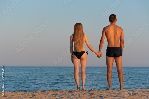 A young couple of lovers look at the sea on the sandy shore