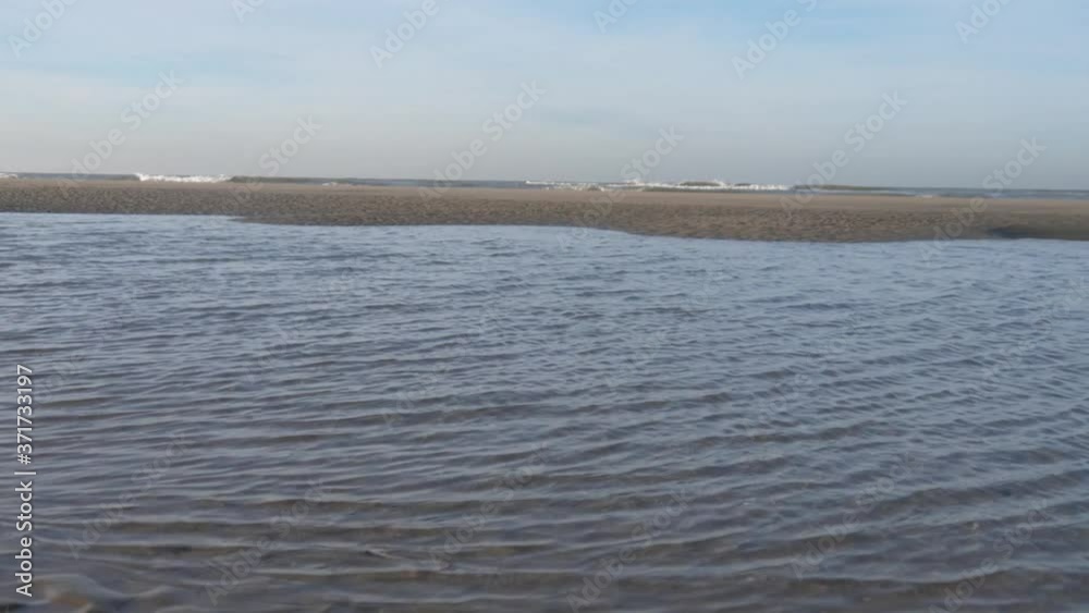 Remnants of water driven by the wind with small waves, view of a sandbank and the surf, behind it the open North Sea and the horizon, a single bird briefly flies through the picture Remnants of water driven by the wind with small waves, view of a sandbank and the surf, behind it the open North Sea and the horizon, a single bird briefly flies through the picture