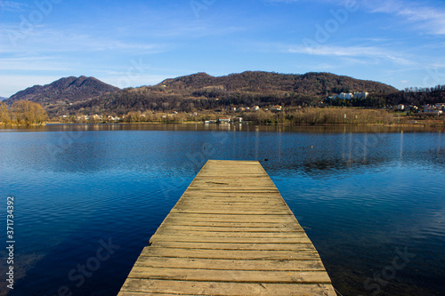 Fishing jetty in the lake of Revine - Wooden pier for mooring boats on Revine Lago, Treviso. Panorama of the lake with rustic jetty and mountains. © JulyLo.Studio