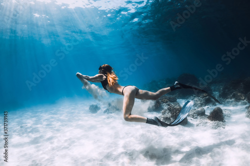 Woman freediver posing over sandy bottom with fins. Freediving in blue ocean at Hawaii