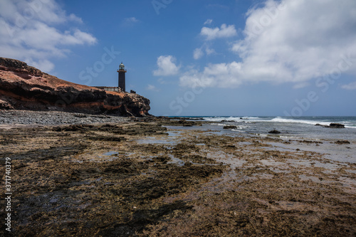 Rocky Atlantic coastline at low tide. In the background, the Punta Jandia lighthouse. Fuerteventura. Canary Islands. Spain.