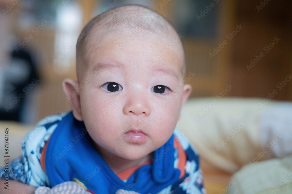 Curious Asian infant baby boy lie on the stomach or prone, wearing white blue clothes on the bed