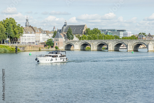 Maas river with a boat sailing, the Servatius bridge (Sint Servaasbrug) and with an urban landscape of the city of Maastricht in the background, sunny day in the South Limburg, Netherlands photo