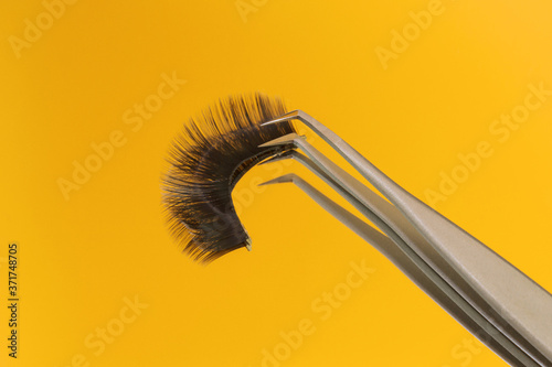 Eyelash tweezer with false eyelashes on a bright yellow background. Place for your text. Minimalism. Beauty concept. Background, texture