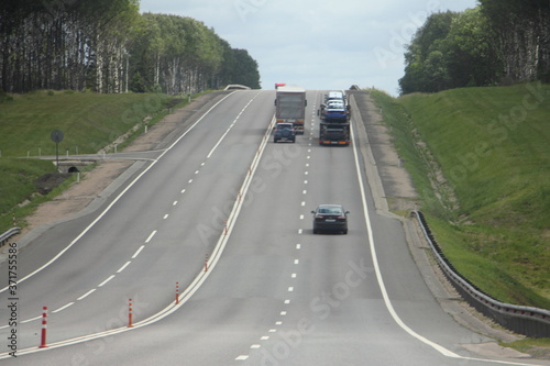 Suburban asphalted 4-lane 2 way road in parspective with overtaking trucks on hill in Europe on summer day on blue sky background with green grass and trees on roadsides, transportation logistics photo