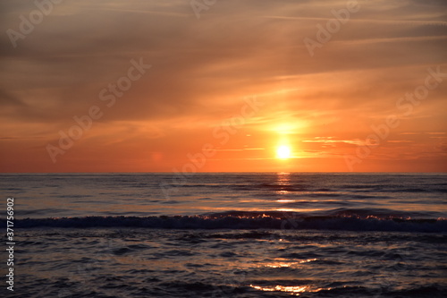 Zachód słońca nad morzem z falami w odcieniach mocnego pomarańczu i czerwieni. © Grzegorz