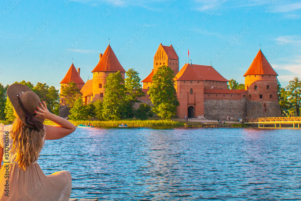Φωτογραφία TRAKAI/LITHUANIA: 09/07/2019: Beautiful girl sitting in front of the colorful Trakai Historical National Park, UNESCO world heritage site, on beautiful summer day