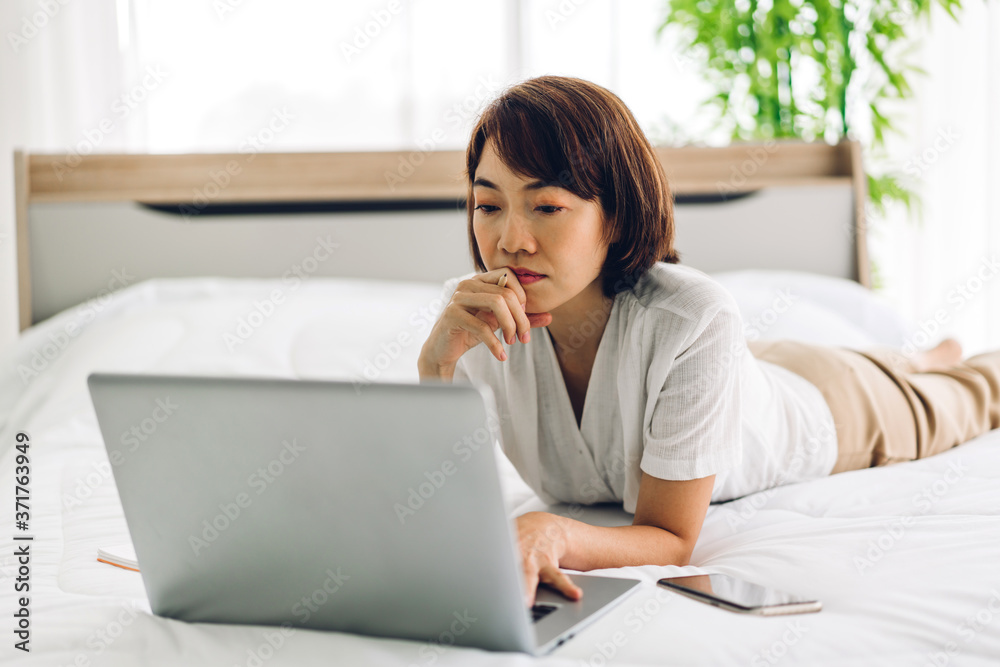 Smiling happy beautiful asian woman relaxing using laptop computer working and video conference meeting on bed at home.work from home concept Smiling happy beautiful asian woman relaxing using laptop computer working and video conference meeting on bed at home.work from home concept