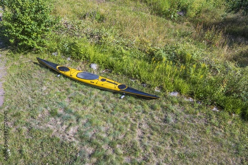 Close up view of yellow kayak isolated on green grass field and green forest trees over blue lake water background.