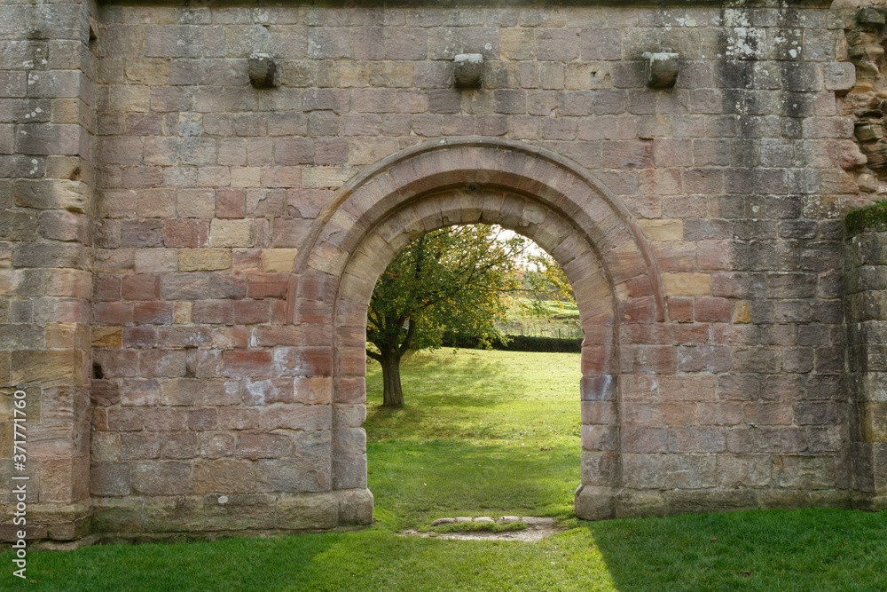 Gothic Archway Leading to an Open Field with a Tree, Fountains Abbey, Ripon, North Yorkshire, England, UK.