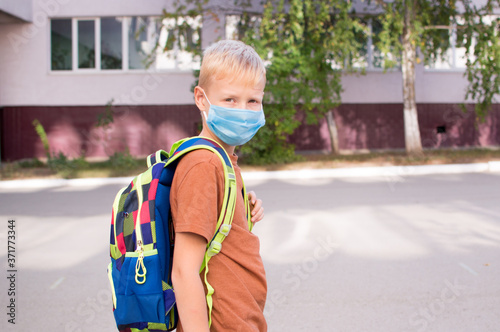 Back to school. School-age boy with a protective medical mask on her on his face with a school backpack. New school year in 2020.C Personal protective equipment.