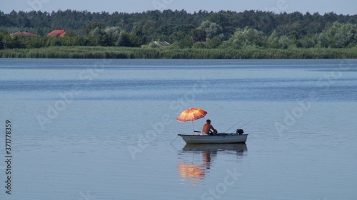 A man on a white boat with an orange umbrella fishing in the river
