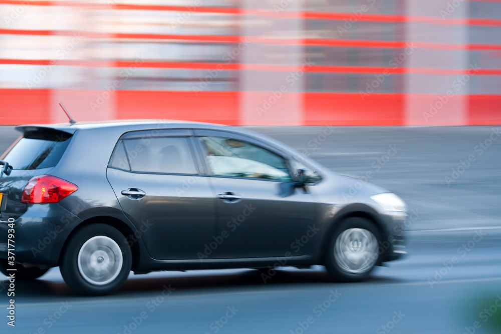 Gray car moving fast along the road on blurred stripped red background