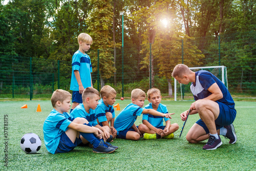 Young coach with clipboard teaches little children the strategy of playing on the football field. 