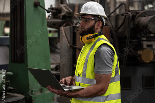 Portrait of technician man or industrial worker with hardhat or helmet, eye protection glasses and vest working electronic machinery on laptop and mechanical in Factory of manufacturing place