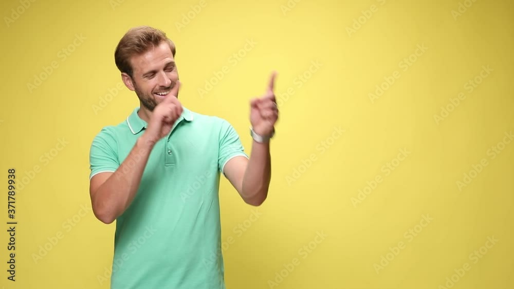 young casual man smiling, rotating arms and pointing fingers to side on yellow background young casual man smiling, rotating arms and pointing fingers to side on yellow background