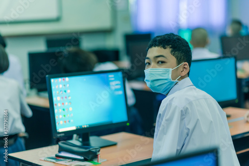 Asian male high school student on the semester start wearing masks in computer classroom during the Coronavirus 2019 (Covid-19) epidemic.