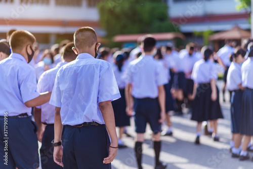 The back view of Asian high school students in white uniforms on the semester start wearing masks during the Coronavirus 2019 (Covid-19) epidemic.