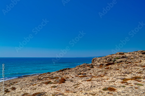 Rocks on the sea coast in the city of Paphos, Cyprus. View of the yellow sand and stone cliffs with shallow desert vegetation.