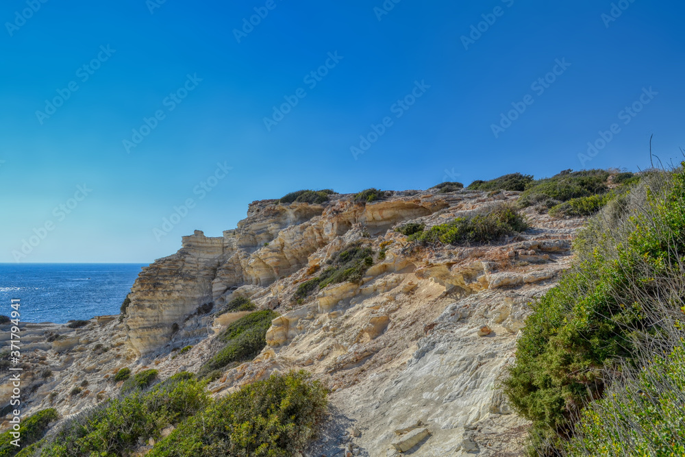 Cliffs on the Mediterranean coast in the city of Paphos, Cyprus.  Light stone blocks surrounded by small vegetation with the sea in the background.