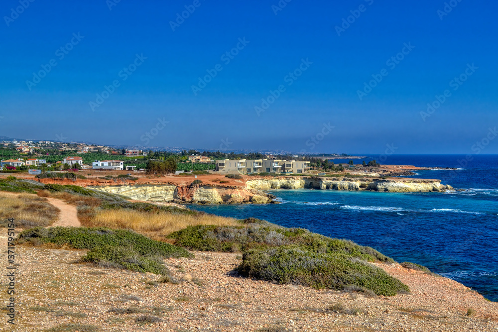 A small lagoon with blue sea water on the coast of Paphos, Cyprus.  In the distance you can see the hotel with the beach.  Waves breaking on coastal cliffs.