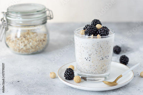 overnight oats with coconut milk, chia seeds, hazelnuts and blackberries on a gray background. healthy diet breakfast. copy space. horizontal image