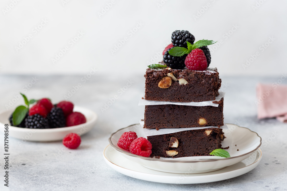 chocolate brownie square pieces with hazelnuts, decorated with raspberries and blackberries. homemade bakery and dessert. Gray background. copy space.