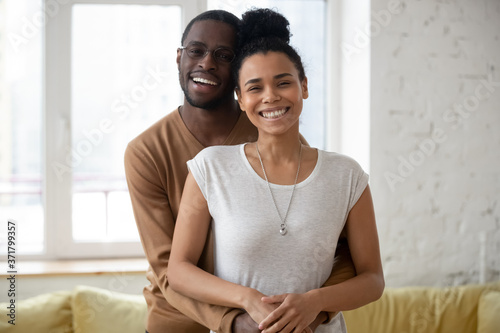 Happy together. Portrait of smiling black married couple buyers of realestate posing in new flat, millennial african guy and girl in love tenants or renters of house hugging warm and looking at camera