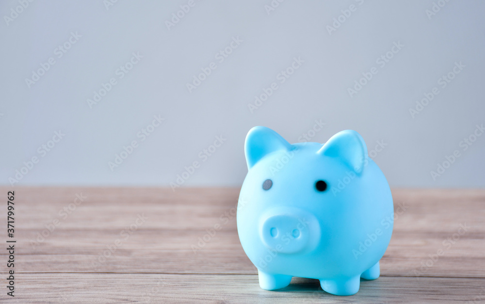 Fototapeta premium A blue piggy bank and a coin on a wooden table to save money .