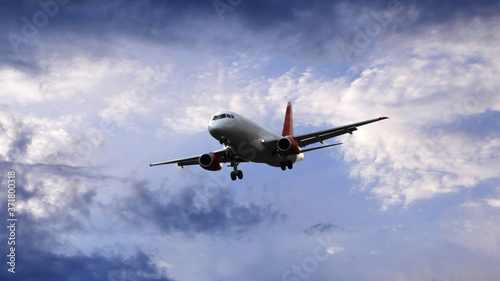 Airplane flying under beautiful evening clouds  front view.