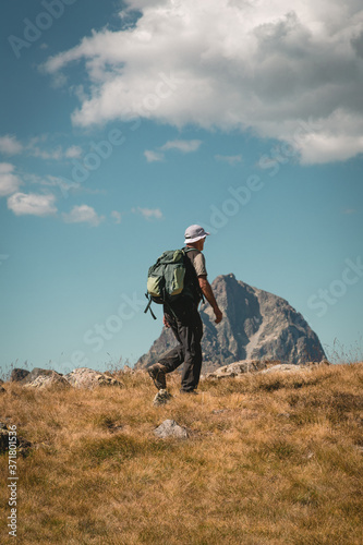 Man with backpack hike to the top of the mountain and dramatic scenery summer landscape wellness selective focus rear view, freedom concept.