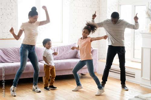 Dancing indoors. Happy black millennial parents and two children daughter and son enjoying dances in living room, active african family dad, mom and kids handle stress of being at home on quarantine
