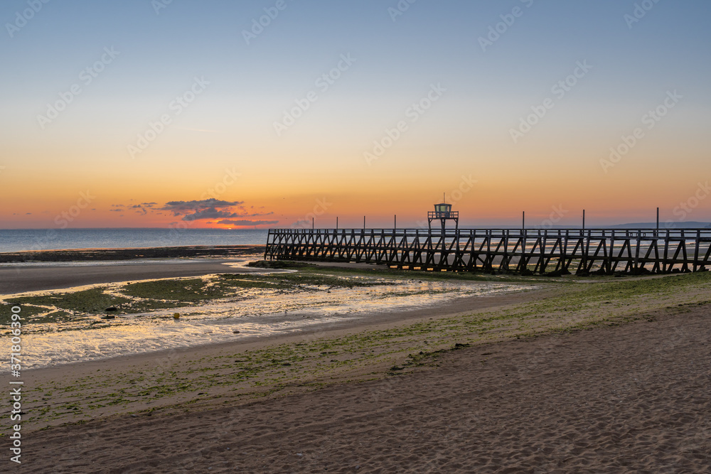Fototapeta premium Luc Sur Mer, France - 08 04 2020: Sunrise over Le Havre and Luc-Sur-Mer pontoon from the beach