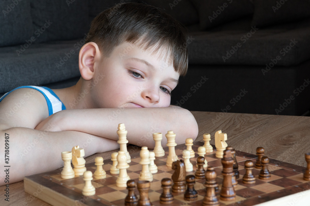 The serious child lost in thought playing chess. Playing board games, on coronavirus quarantine. The child playing chess.