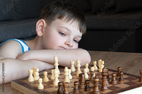 Obraz na płótnie The serious child lost in thought playing chess. Playing board games, on coronavirus quarantine. The child playing chess. w salonie